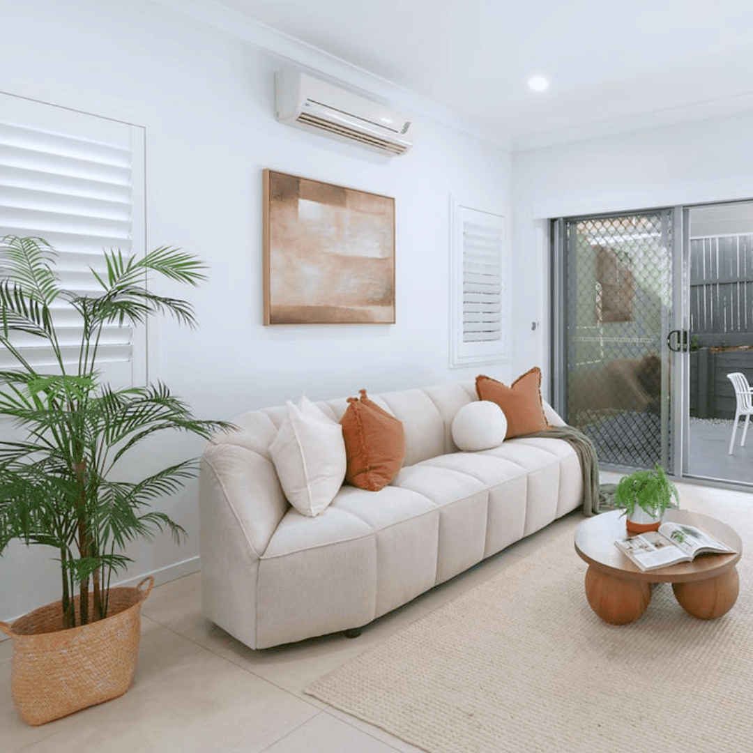 Neutral investment property living room furnished with a sofa, plants and warm accent cushions